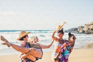 Gruppo allegro di ragazzi e ragazze di persone si divertono insieme in spiaggia durante le vacanze estive - uomini che trasportano donne - clotehs colorati per il concetto di stile di vita del mare all'aperto