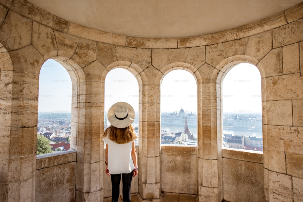 Young woman tourist enjoying cityscape view from the terrace with arches traveling in Budapest, Hungary