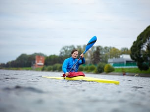 Young concentrated Caucasian sportsman in swimming jacket paddling down the channel in yellow kayak during training