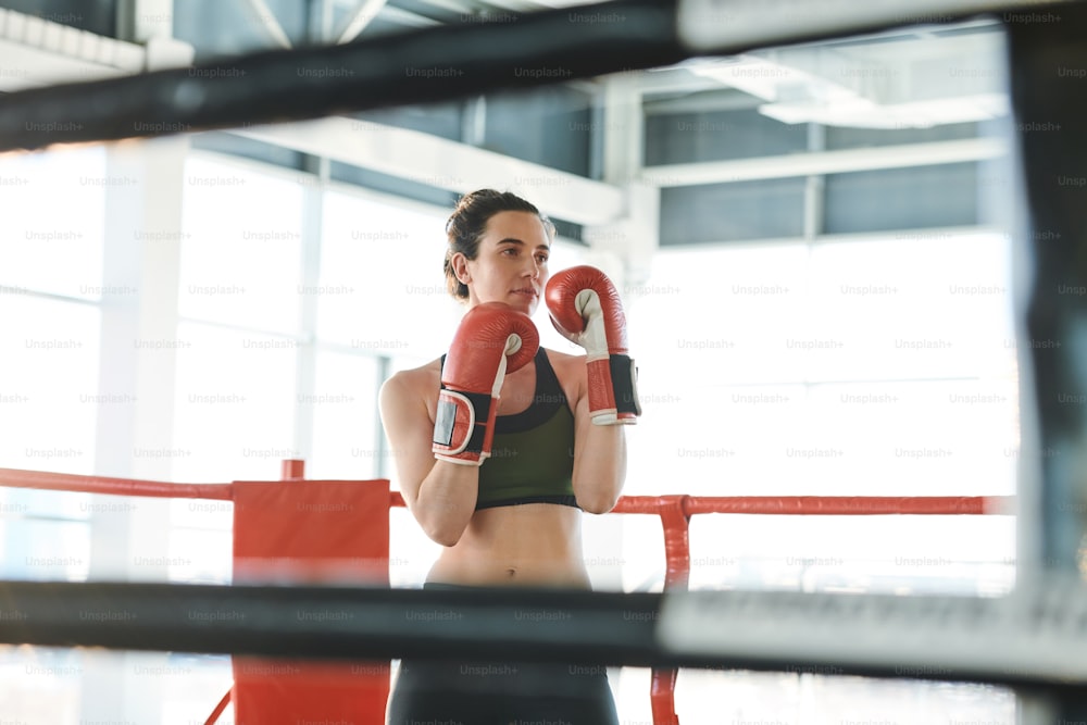 Young strong woman ready to fight her rival standing on boxing ring with hands in front of her