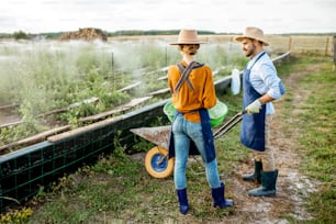 Well-dressed farmers standing on the farmland with green buckets for feeding snails on a farm outdoors. Concept of agribusiness and farming