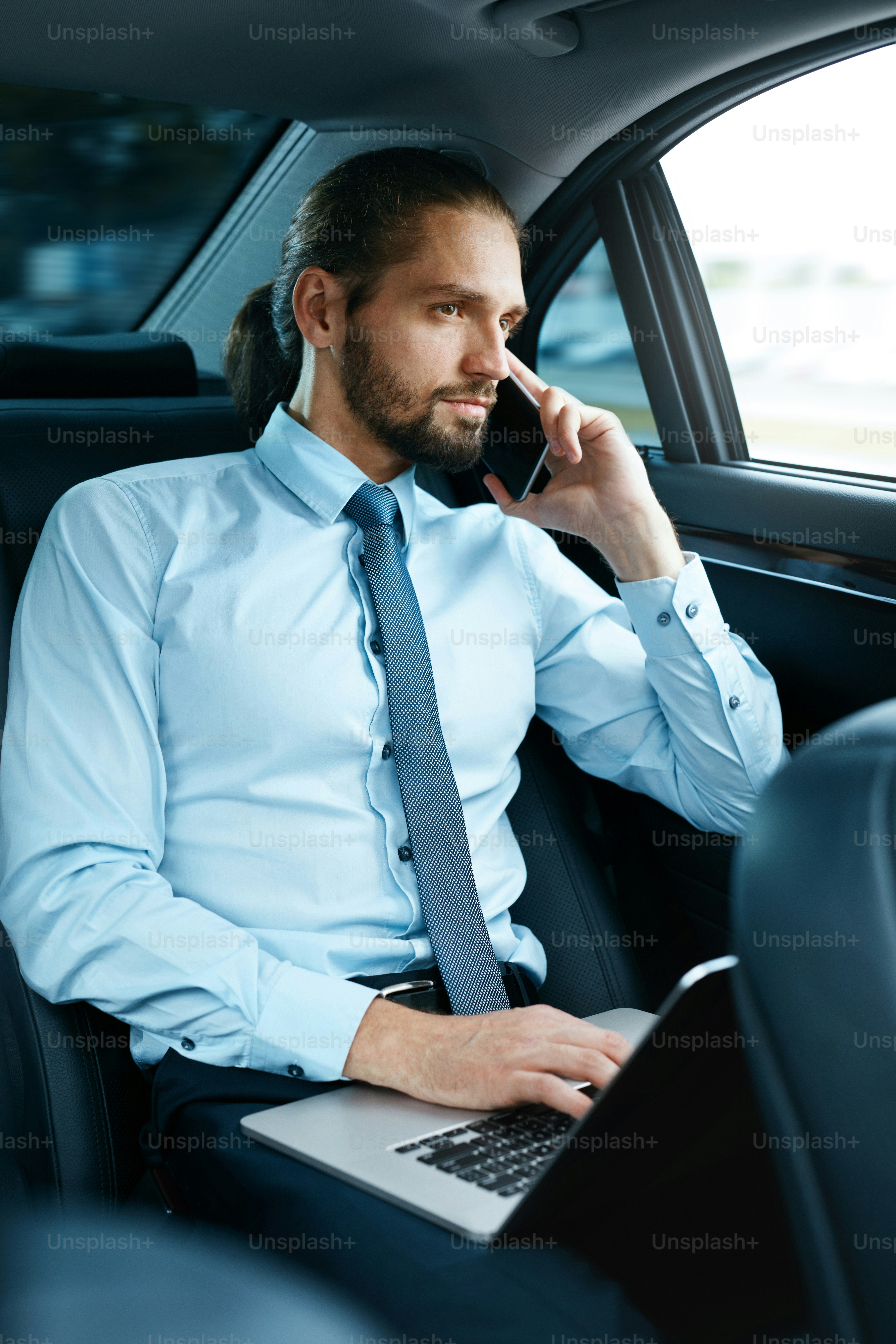 Homem de negócios no carro ligando no telefone enquanto vai trabalhar. Bonito sorridente jovem macho falando no smartphone, sentado no banco de trás do carro de negócios. Imagem de alta qualidade.