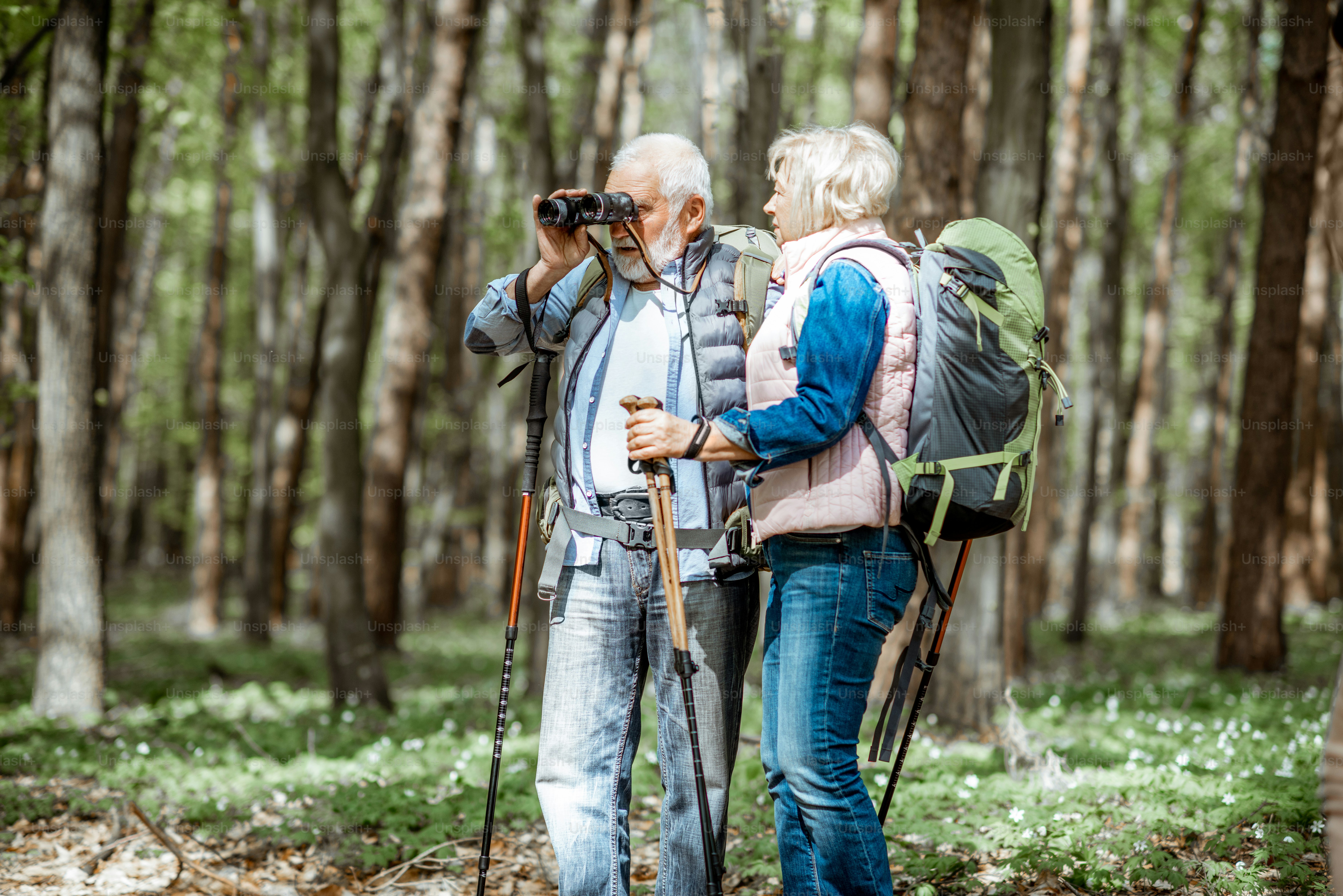 Senior couple looking with binoculars while hiking in the forest. Concept of an active lifestyle on retirement