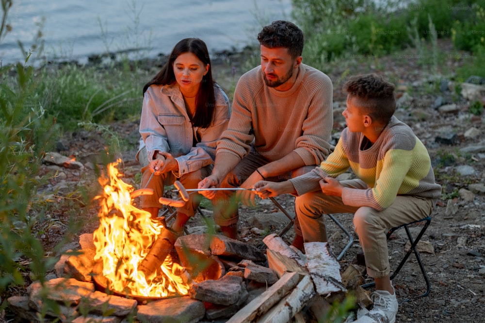 Trois jeunes routards font frire des saucisses sur un feu de camp le soir