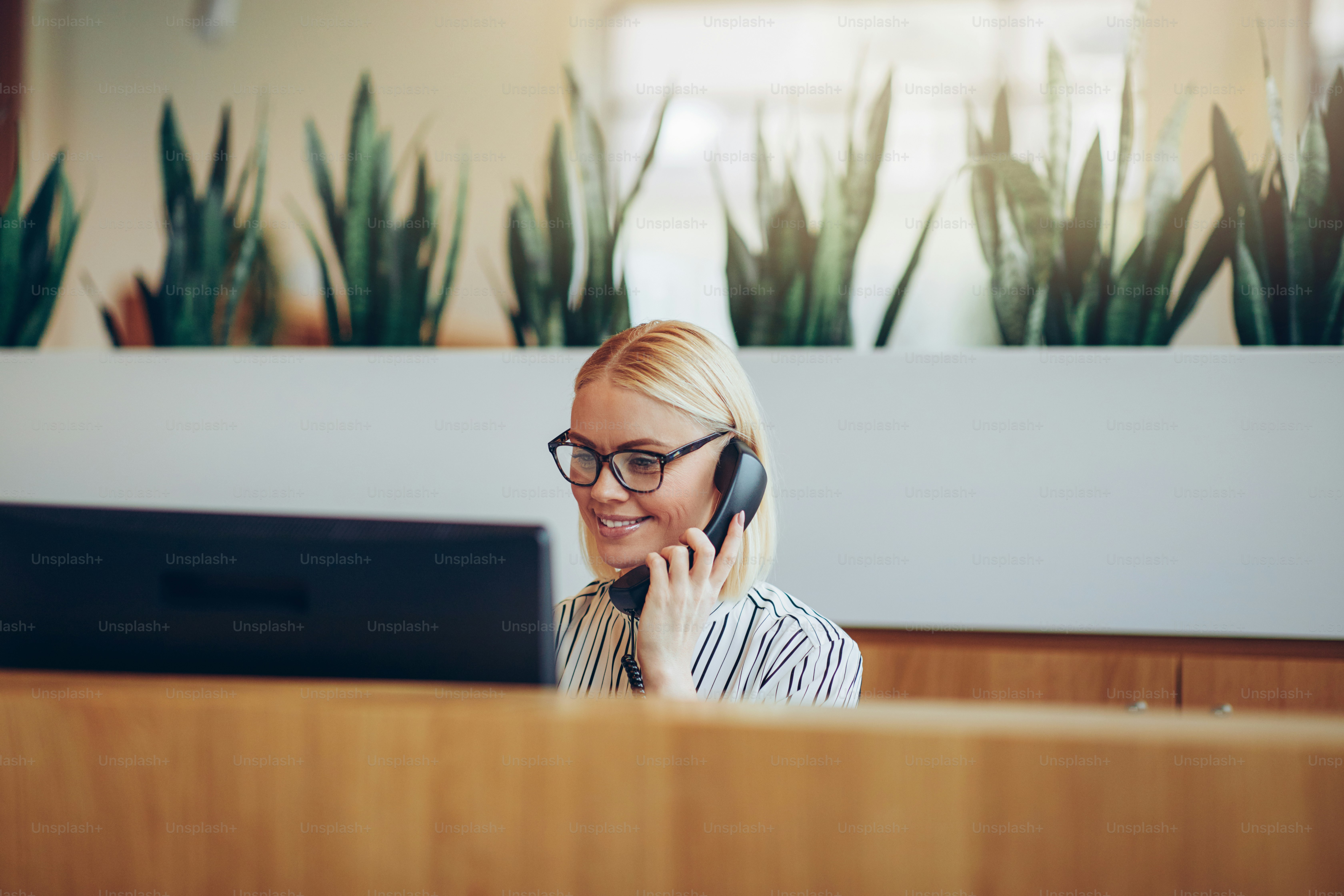 Smiling young businesswoman talking with a client on the telephone while working on a computer at her desk in a bright modern office
