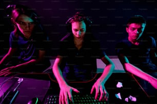 Grupo de jóvenes jugadores contemporáneos de videojuegos de ciberdeportes con auriculares que desarrollan un nuevo juego mientras uno de ellos escribe en el teclado