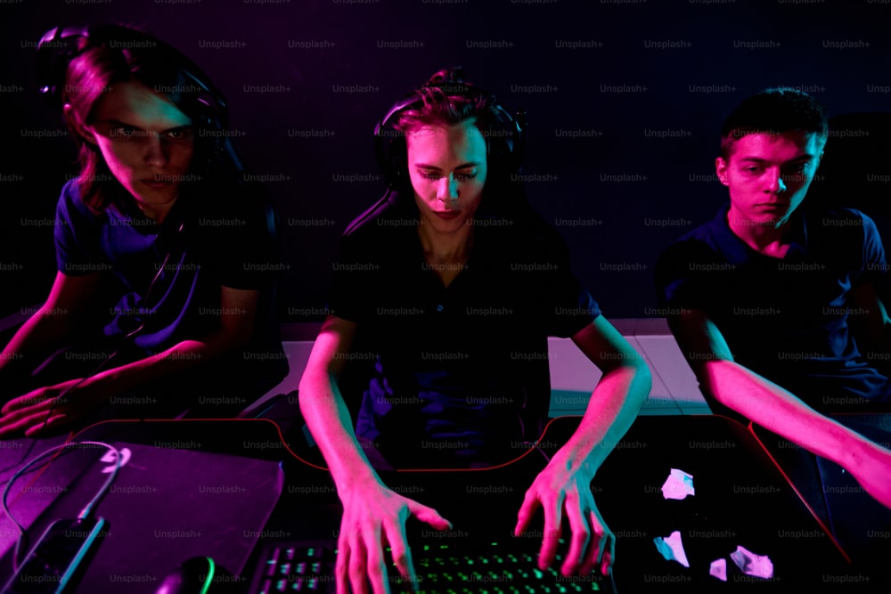 Group of young contemporary cybersports video gamers with headsets developing new game while one of them typing on keyboard