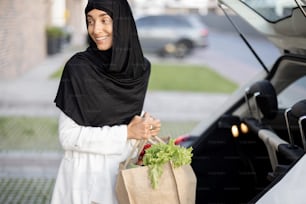 Mulher de negócios muçulmana jovem em hijab indo para casa com mantimentos, de pé com saco de compras na varanda de sua casa