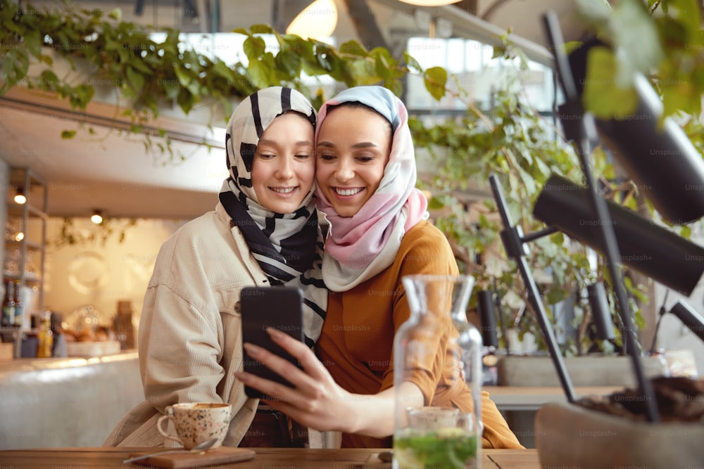 Women. Girls In Hijab Taking Selfie. Friends Meeting In Cafe. Smiling Muslim Female Having Fun In Bistro.