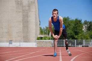 Portrait of adaptive sportsman with prosthetic foot training on running track at the stadium on sunny summer day. Real bodies, diversity, recovery, adaptive sportsman training concept