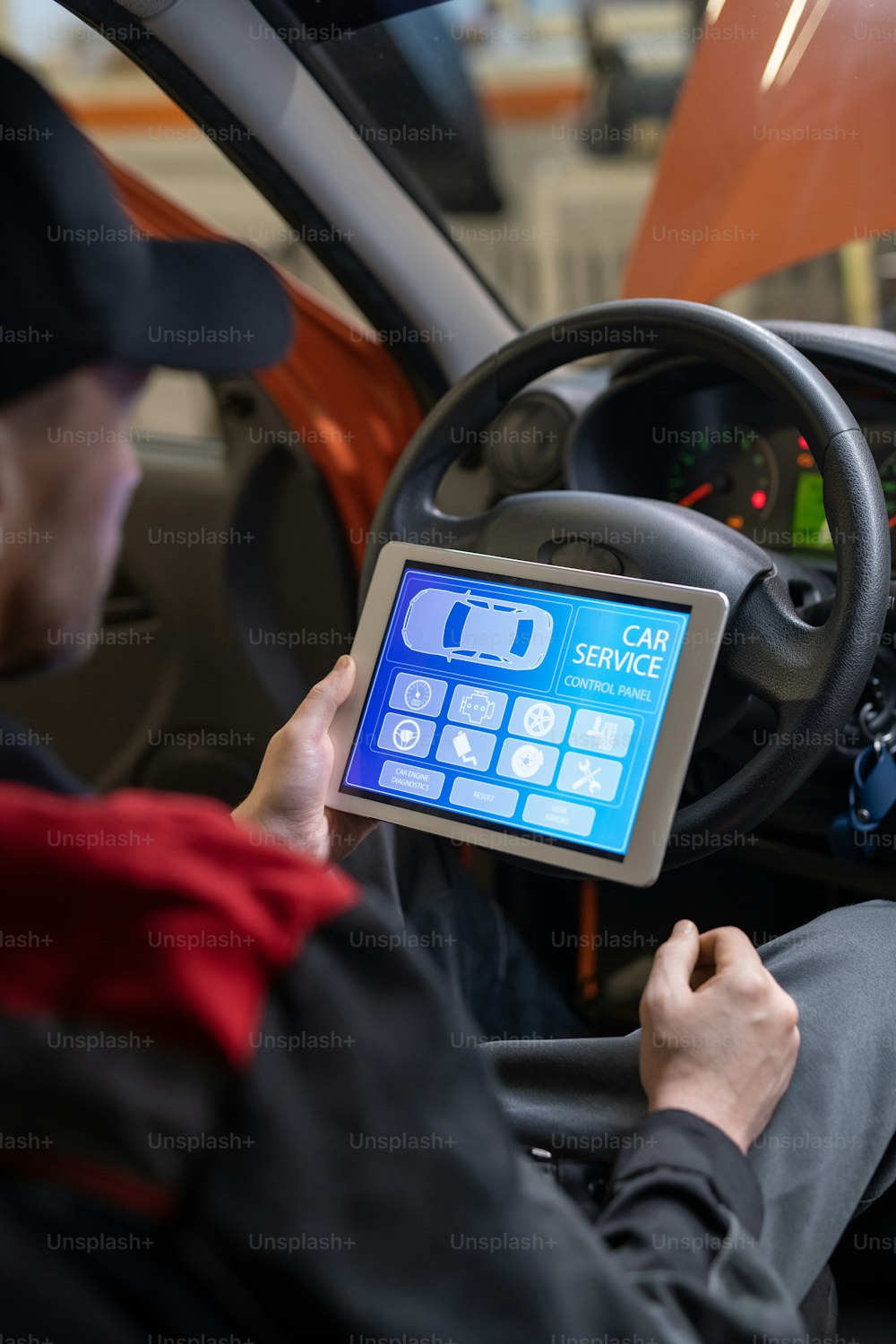 Young repairman with digital tablet sitting in front of steer and looking at icons and options on home page of car service website on screen