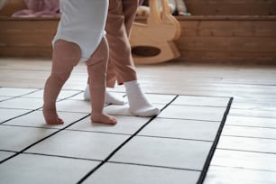 알아볼 수 없는 젊은 어머니가 집에서 아기에게 걷기를 가르치는 시간을 보내는 낮은 섹션 샷