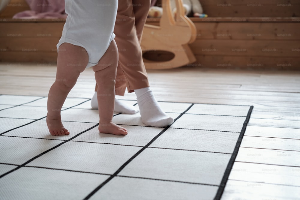 Inquadratura in sezione bassa di una giovane madre irriconoscibile che trascorre del tempo a casa insegnando al suo bambino a camminare