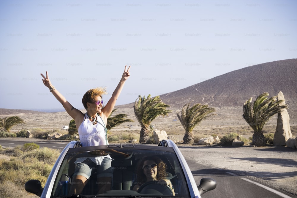 Coppia di donna felice godersi il viaggio viaggiando in auto - guidando e stando fuori dal tetto con il successo e la felicità posa - vacanza in luogo tropicale all'aperto per persone allegre