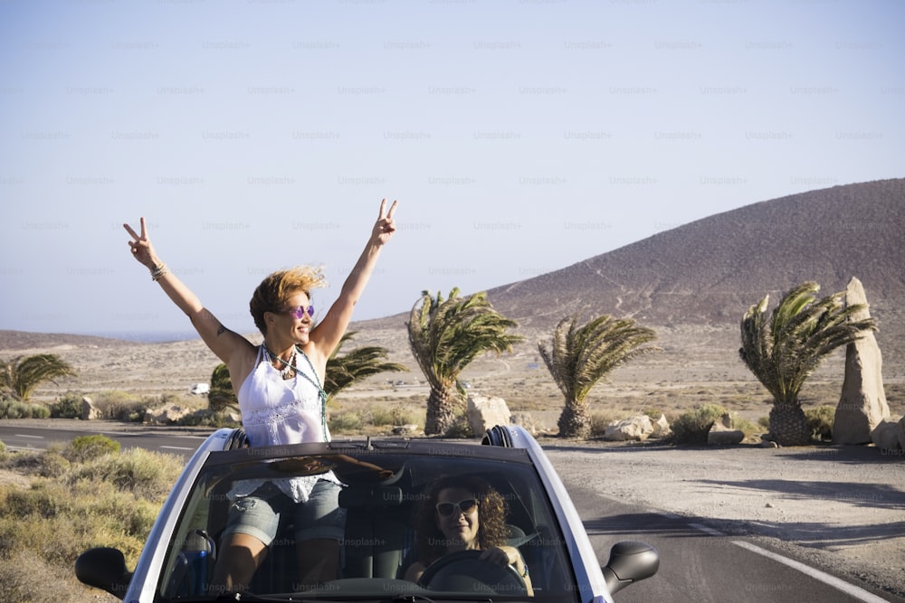 Couple of happy woman enjoy the trip traveling by car - driving and standing outside the roof with success and happiness pose - vacation in outdoor tropical place for cheerful people