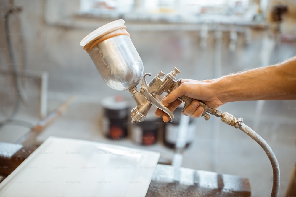 Painting wooden product with a spray gun at the painting shop of the carpentry, close-up