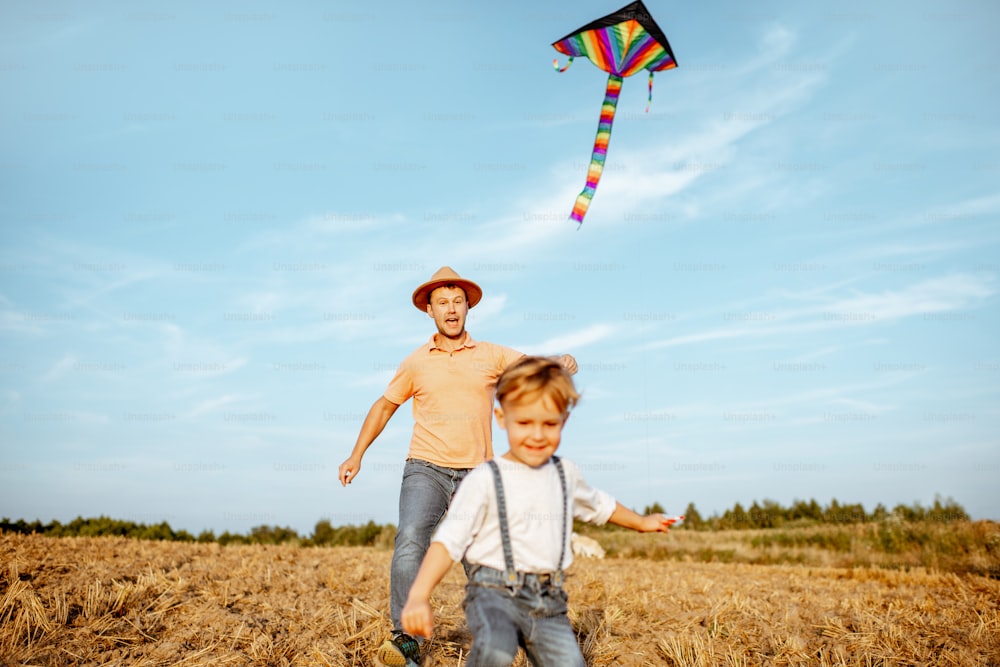 Padre con hijo corriendo mientras lanzan coloridas cometas de aire en el campo. Concepto de una familia feliz divirtiéndose durante la actividad de verano