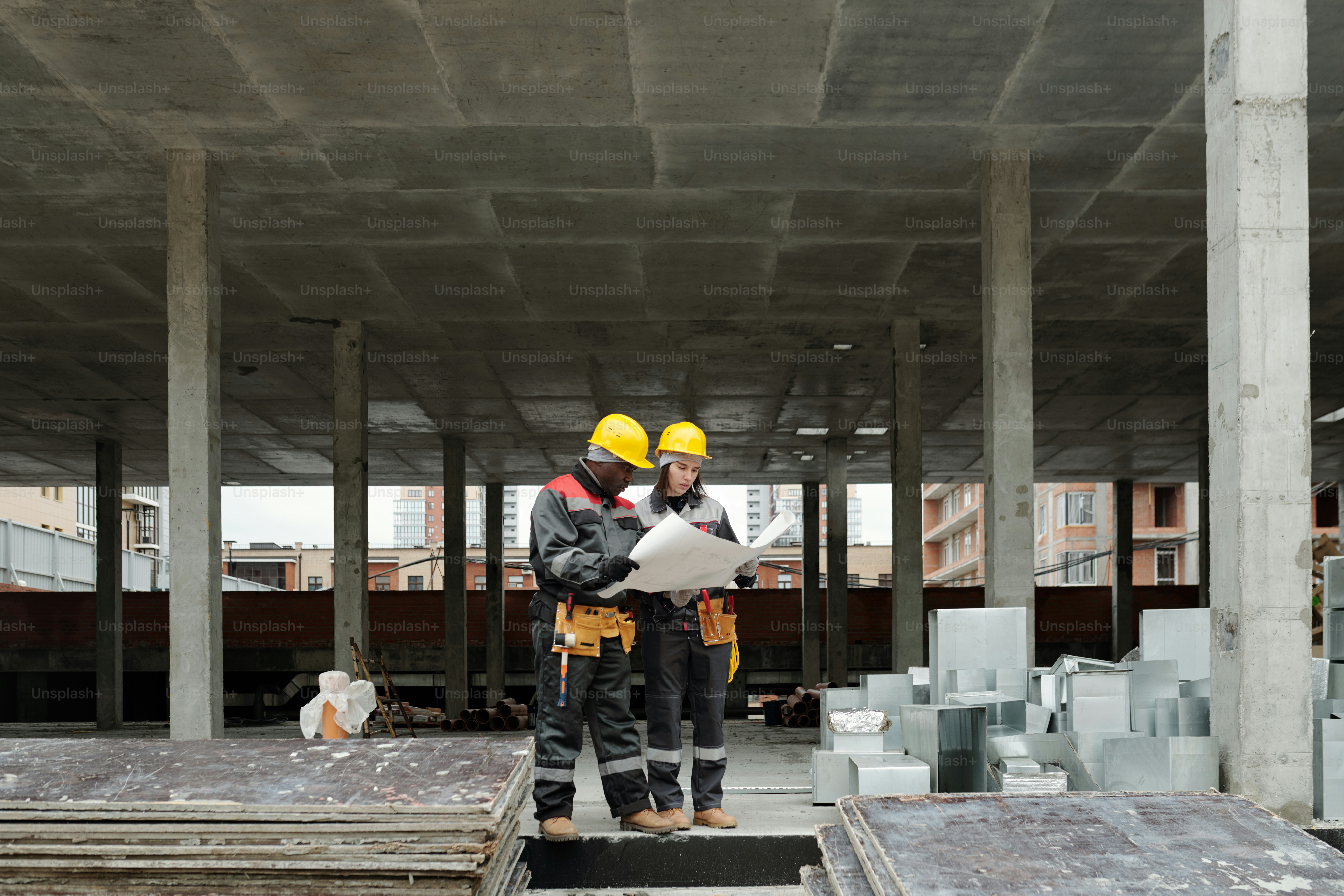 Kleine Gruppe von interkulturellen Ingenieuren oder Bauarbeitern in Arbeitskleidung, die sich den Bauplan auf dem ungerollten Bauplan ansehen und diskutieren