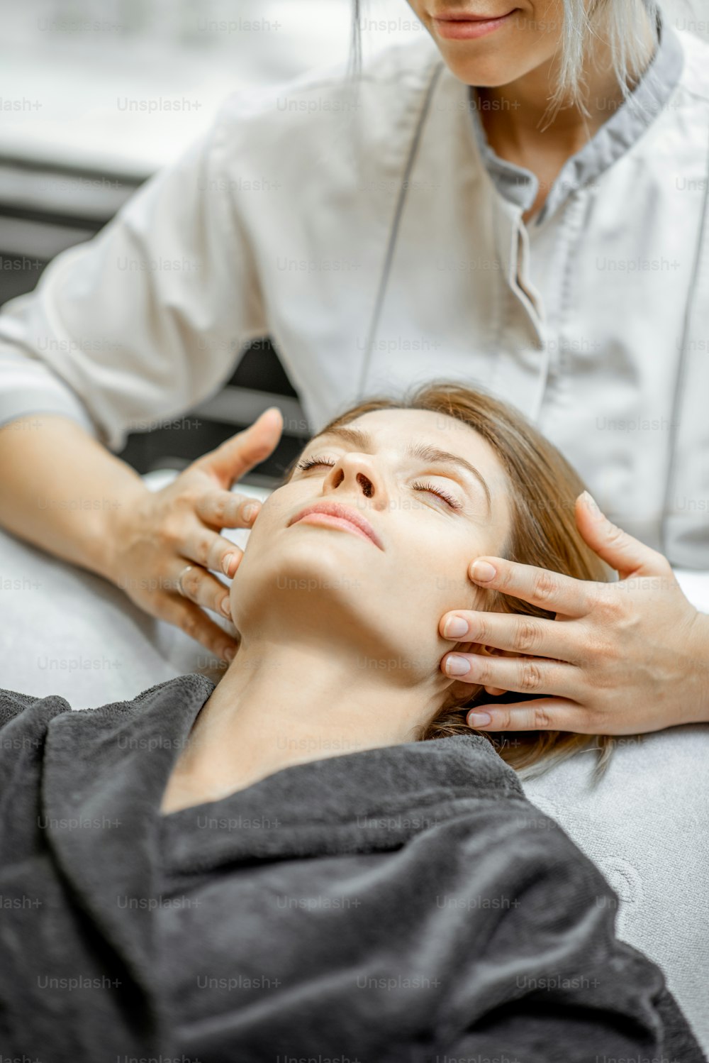 Cosmetologist making facial massage to a beautiful woman at the beauty salon. Concept of a lymph drainage therapy