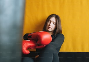 黒の服を着た若い疲れたブルネットの女性は、フィットネスクラブのジムでボクシングのトレーニングに従事しています