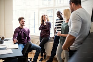 Grupo sonriente de diversos diseñadores jóvenes que hablan juntos en una oficina después de una reunión en la sala de juntas