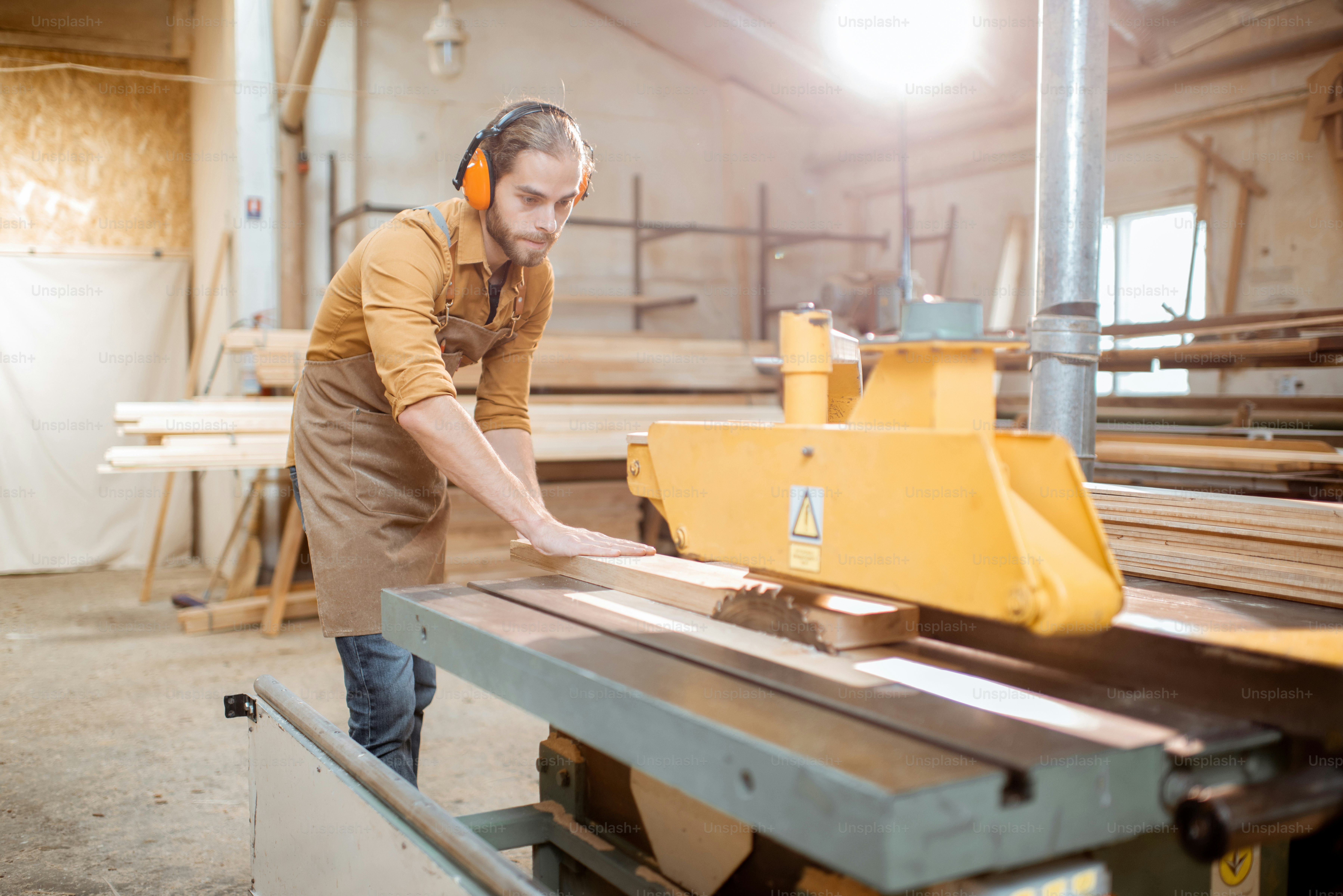 Carpentry worker sawing wooden planks with circular saw in the joinery