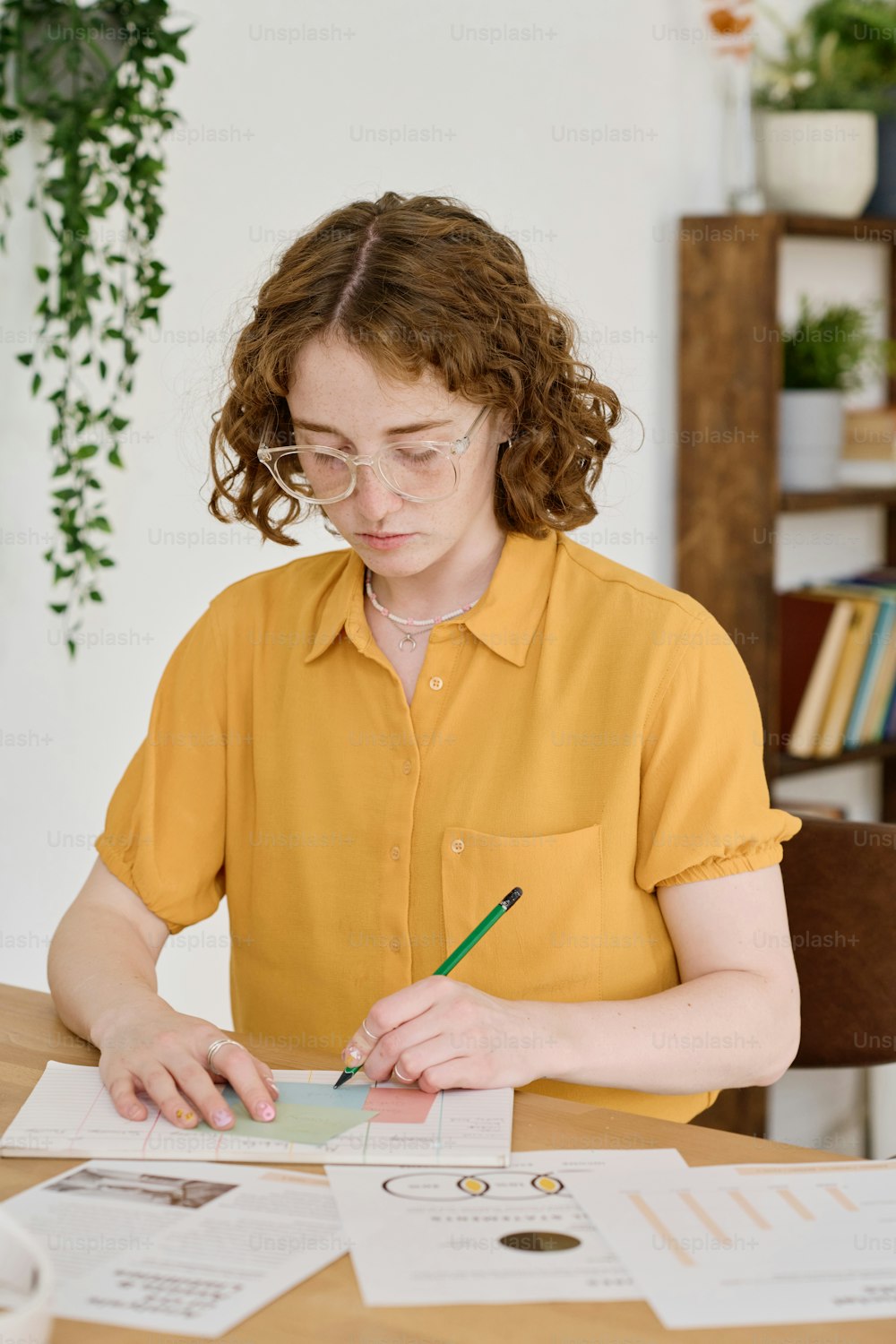 Young serious freelance specialist with pencil drawing working schemes on paper while sitting by workplace in front of camera