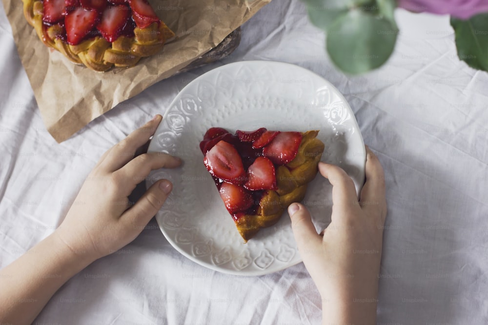 Torta de morango caseira nas mãos da criança na mesa de jantar
