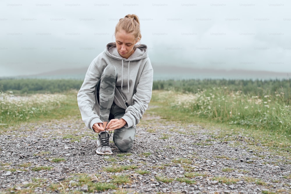 Mid age woman tying shoelaces , getting ready for work out outdoor, she is at the country road with scenic view
