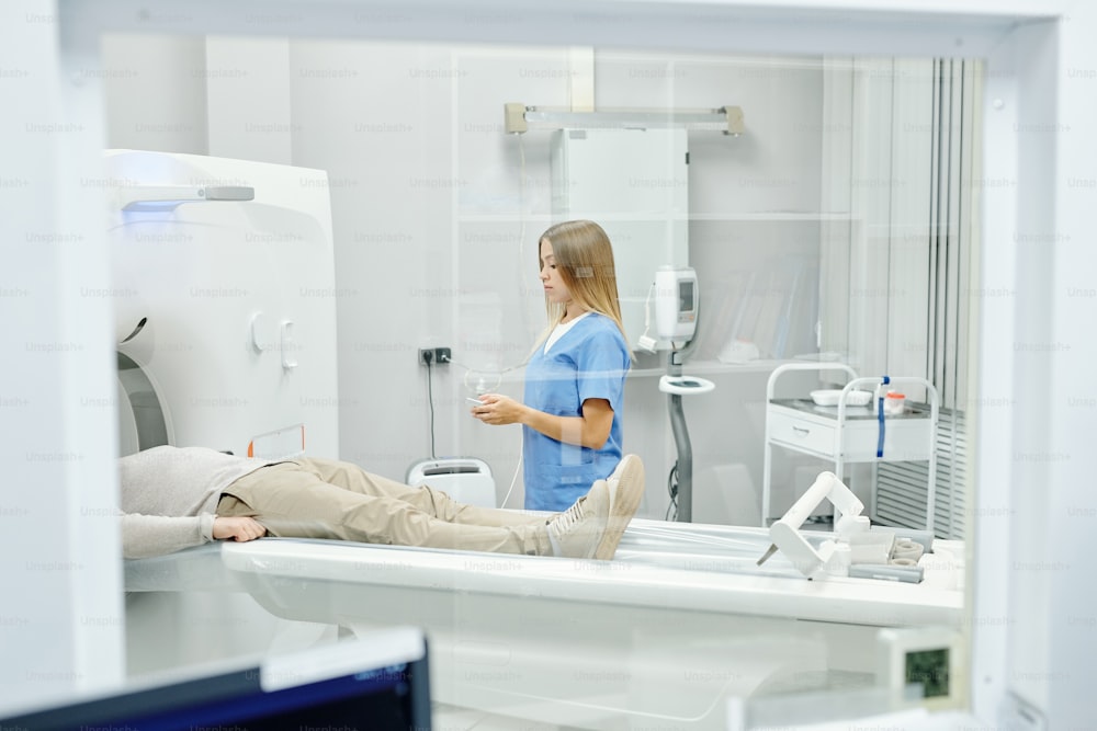 診療所での診察中にクシェットに横たわる男性患者と超音波装置のそばに立つ青い制服を着た若い女性医師