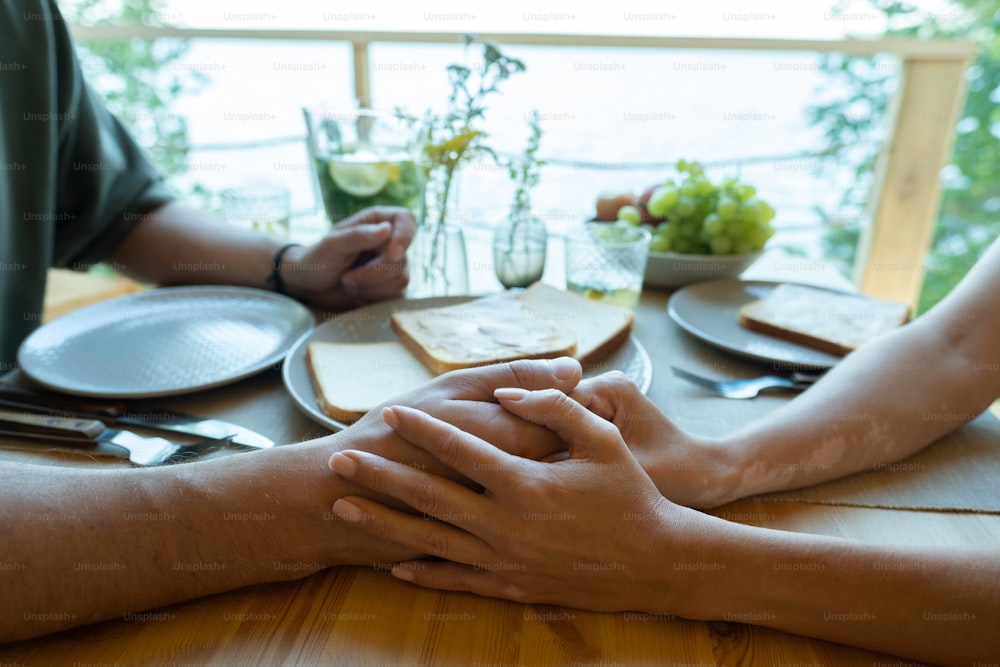 Hands of young affectionate couple sitting by served table while having dinner or breakfast
