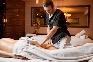 Terapeuta professionista che fa un massaggio profondo a un cliente di sesso maschile nel salone Spa. Lavorare sulla parte inferiore del corpo