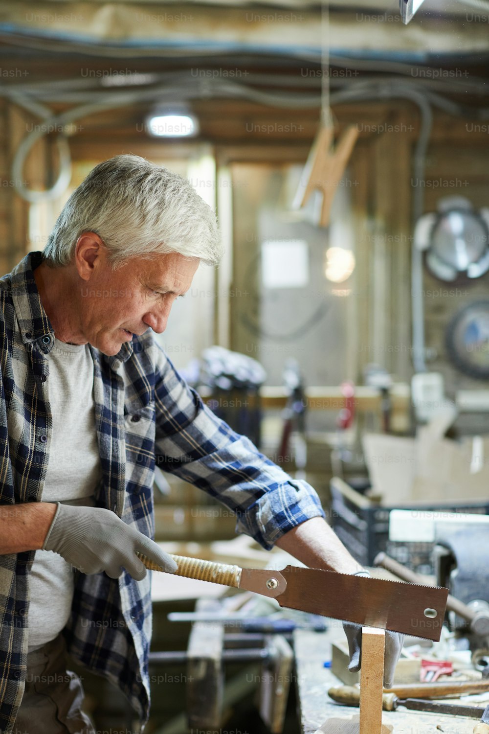 成熟した木工マスターは、手のこぎりで木製のワークピースを鋸で挽く