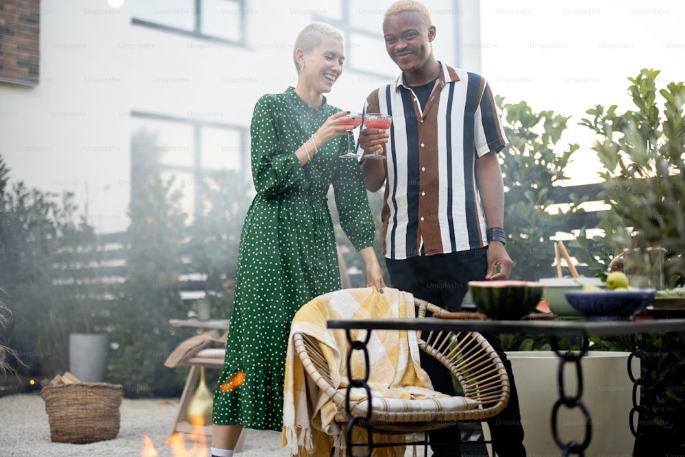 Multiracial couple hanging out together during a dinner at their backyard in the evening. Clinking glasses and having fun. Concept of relationship. Black man and european woman enjoying time together