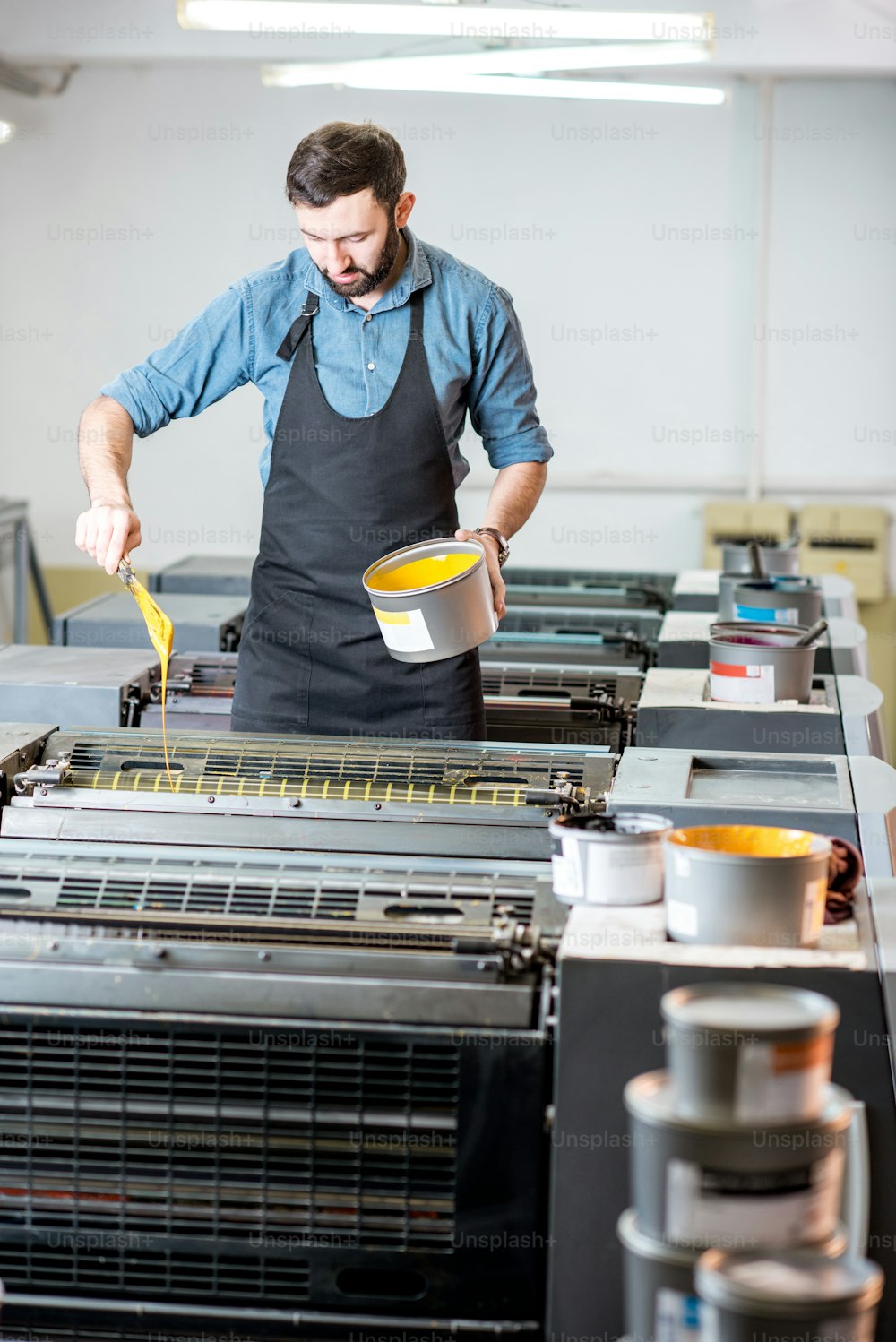Tipógrafo rellenando pintura amarilla en la máquina offset en la fabricación de impresión
