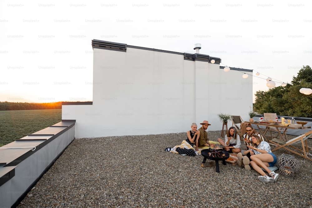Bella terrazza sul tetto di una casa di campagna con gli amici che fanno un picnic, seduti insieme accanto al fuoco