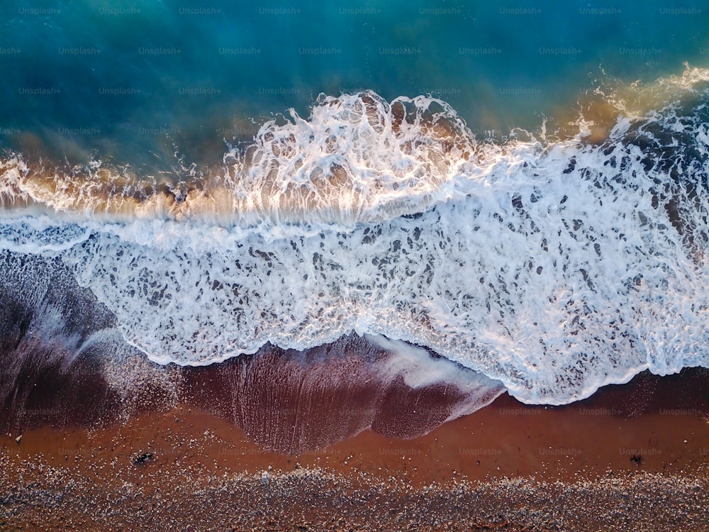 ターコイズブルーの水と砂利浜に近づく波のある紺碧の珊瑚海の風景の空飛ぶドローンからのトップ写真。