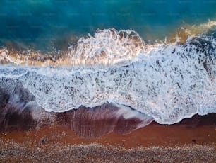 Vista de la foto superior desde un dron volador del paisaje marino de coral azul con agua turquesa y olas que se acercan a la playa de grava.
