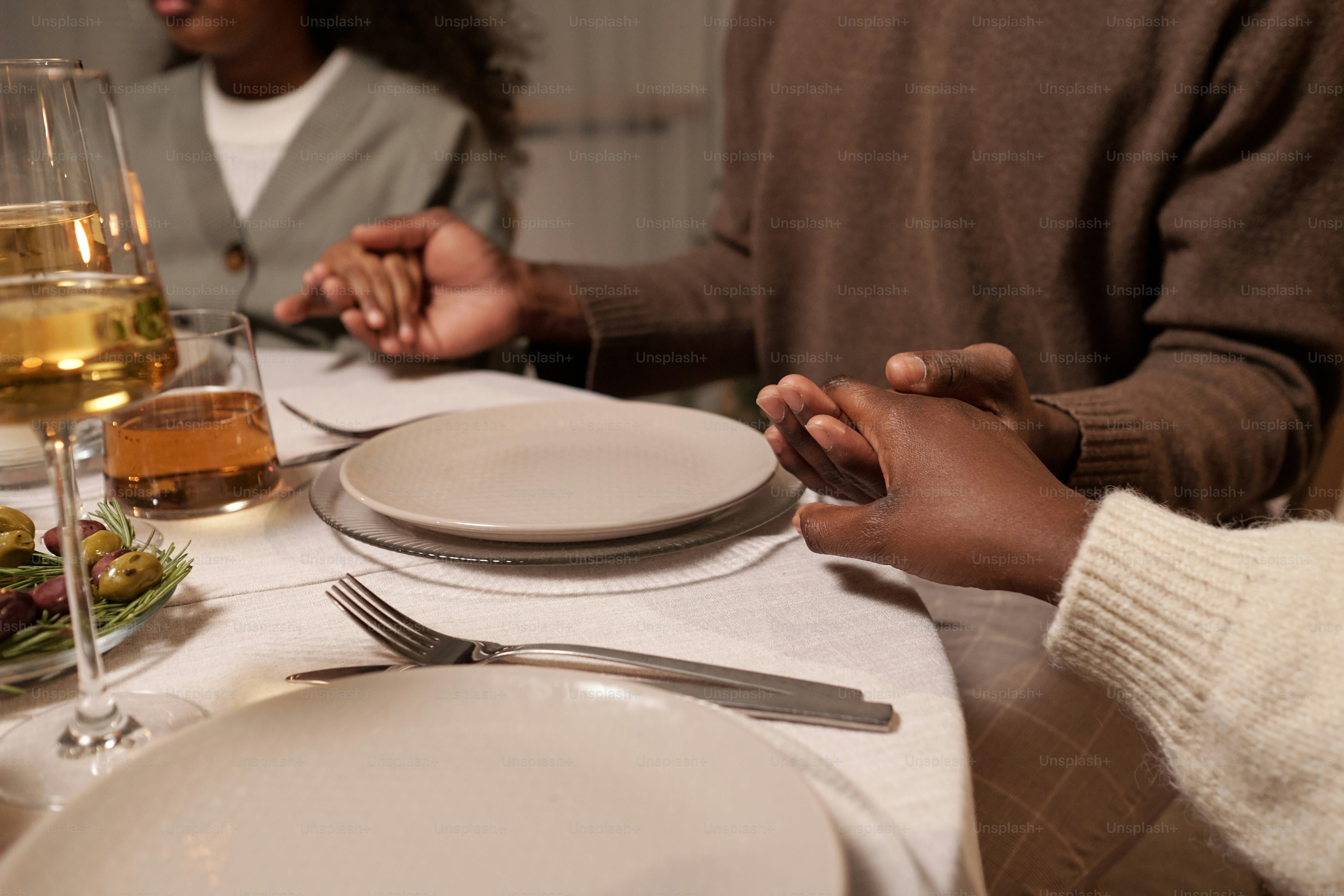 Young couple and their daughter holding by hands while sitting by served festive table and praying before dinner