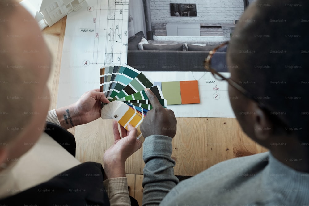 Joven diseñador africano señala la paleta de colores mientras ayuda a su colega femenina durante el trabajo en un nuevo proyecto