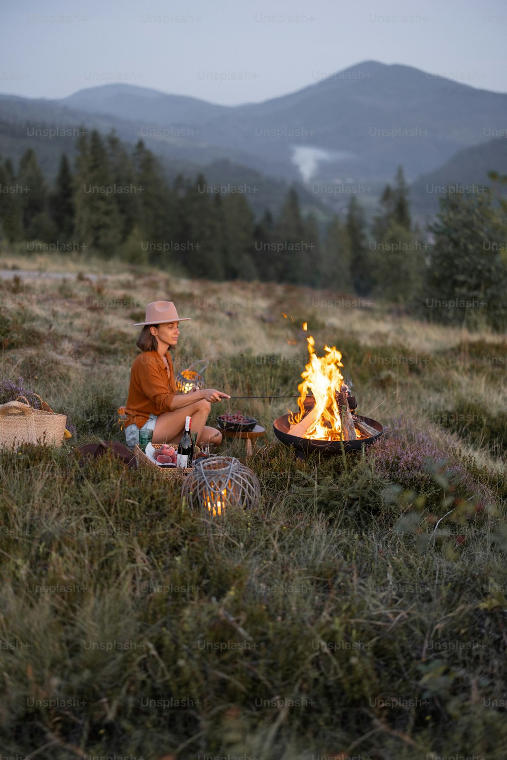 Junge Frau genießt Lagerfeuer während eines Picknicks in den Bergen in der Abenddämmerung. Einsamkeit in der Natur und Reisen in den Bergen Konzept