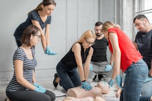 실내에서 훈련하는 동안 인형으로 응급 처치 심장 압박을 하는 방법을 배우는 사람들의 그룹