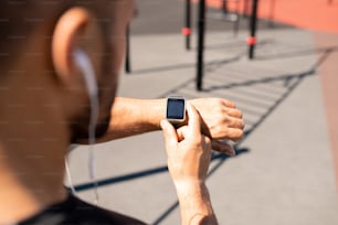 현대 젊은 남성 운동 선수는 경기장에서 달리기 전에 시간을 발견하면서 손목에 스마트 워치를 보고 있습니다.