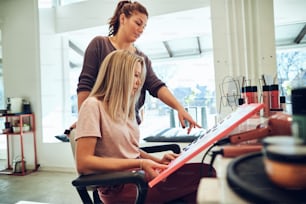 Young blonde woman looking through hair dye samples in a book with her hairstylist while sitting in a salon chair