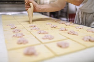 Close up de padeiro trabalhador enchendo pastelaria com delicioso creme. Interior da padaria.