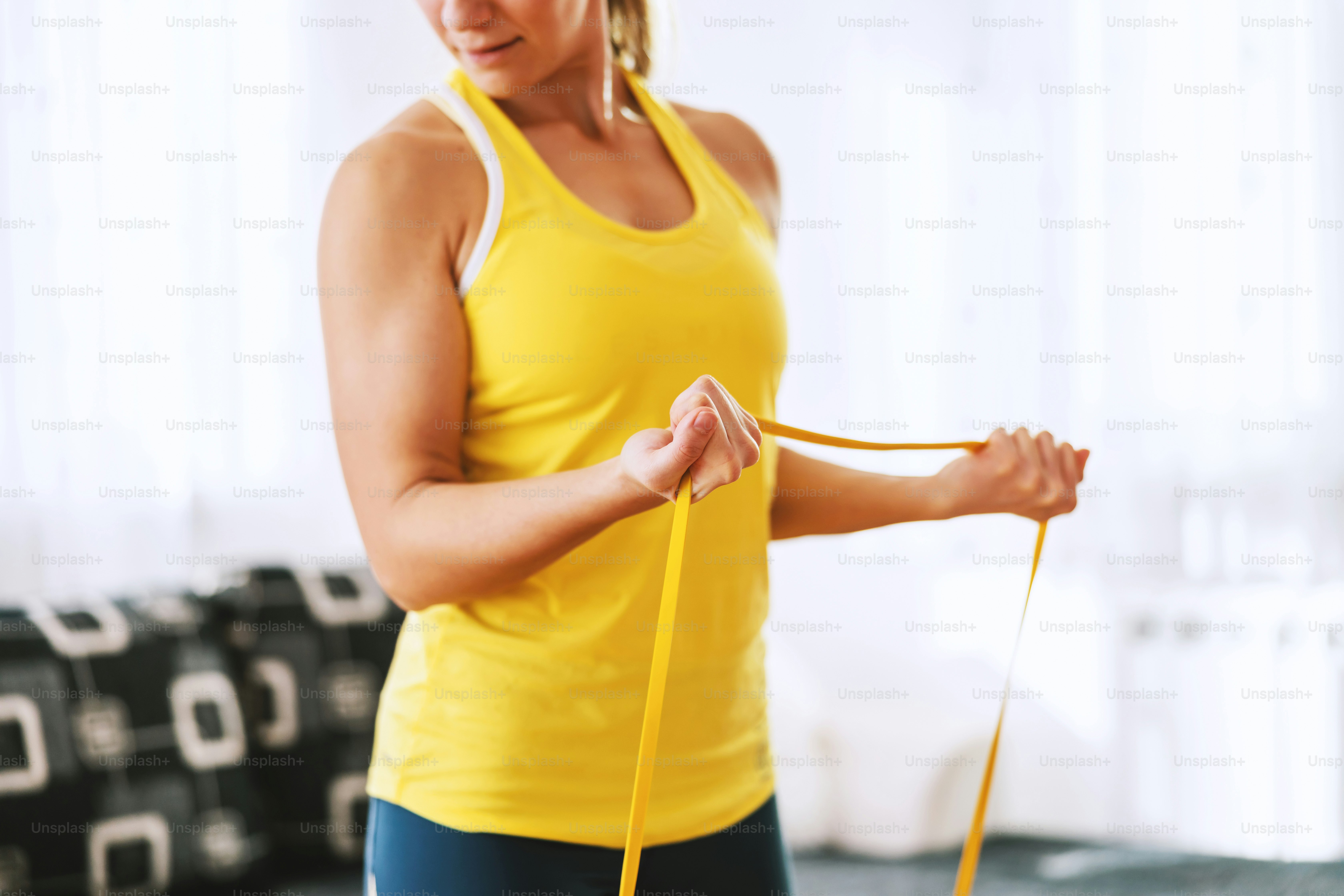 Close up of sportswoman standing and holding power rubber. She is preparing for fitness exercises. Home interior.