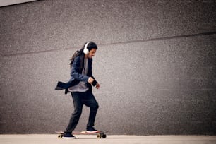 Young stylish man with dreadlocks is listening to music and riding his longboard.