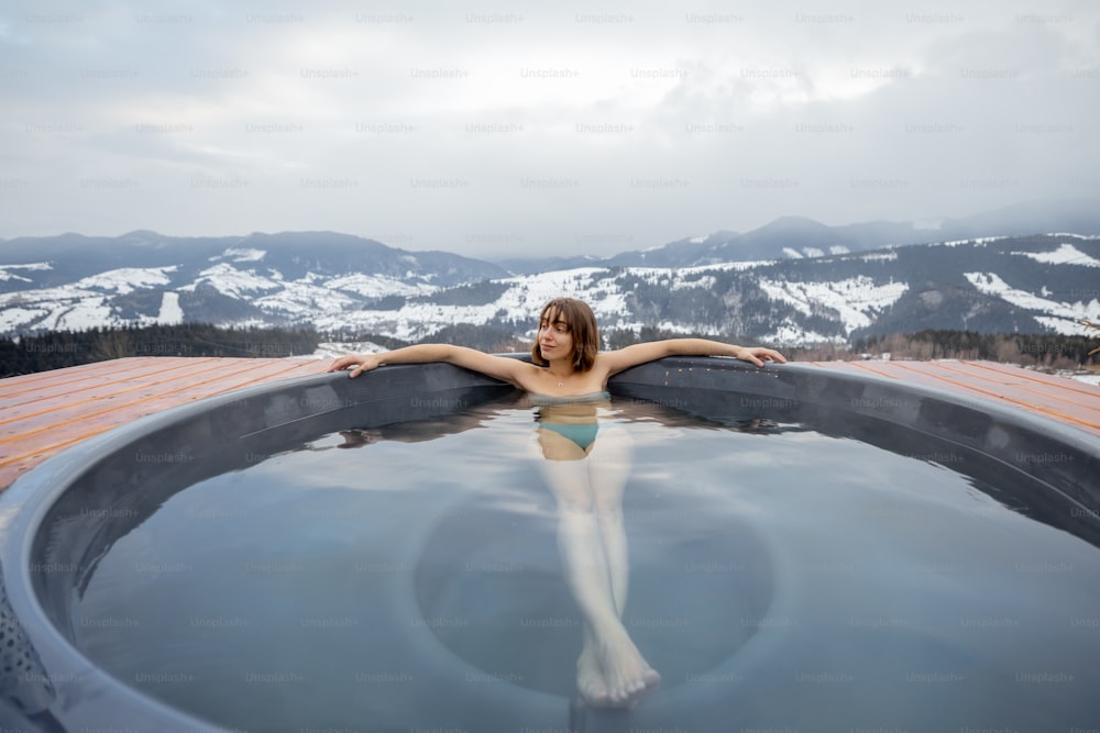 Mujer joven bañándose en bañera de hidromasaje en las montañas durante el invierno. Concepto de descanso y recuperación en cuba caliente en la naturaleza. Idea de evasión y recreación en las montañas