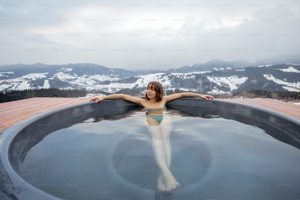 Junge Frau beim Baden im Whirlpool in den Bergen im Winter. Konzept der Ruhe und Erholung in heißem Bottich auf der Natur. Idee von Flucht und Erholung in den Bergen