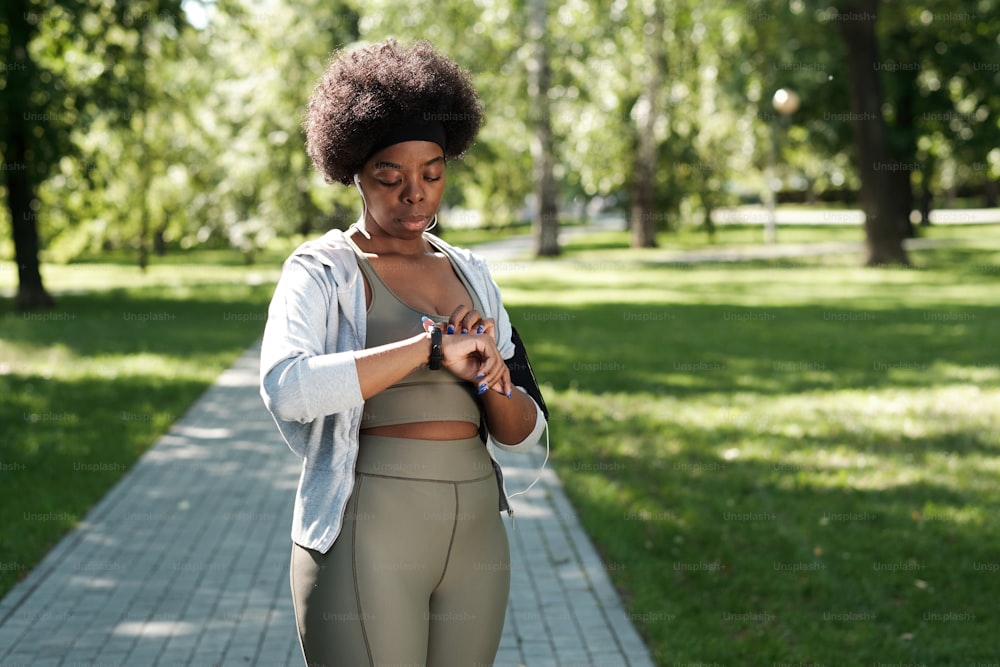 Jeune femme sportive regardant une montre intelligente au poignet tout en se tenant debout dans le parc